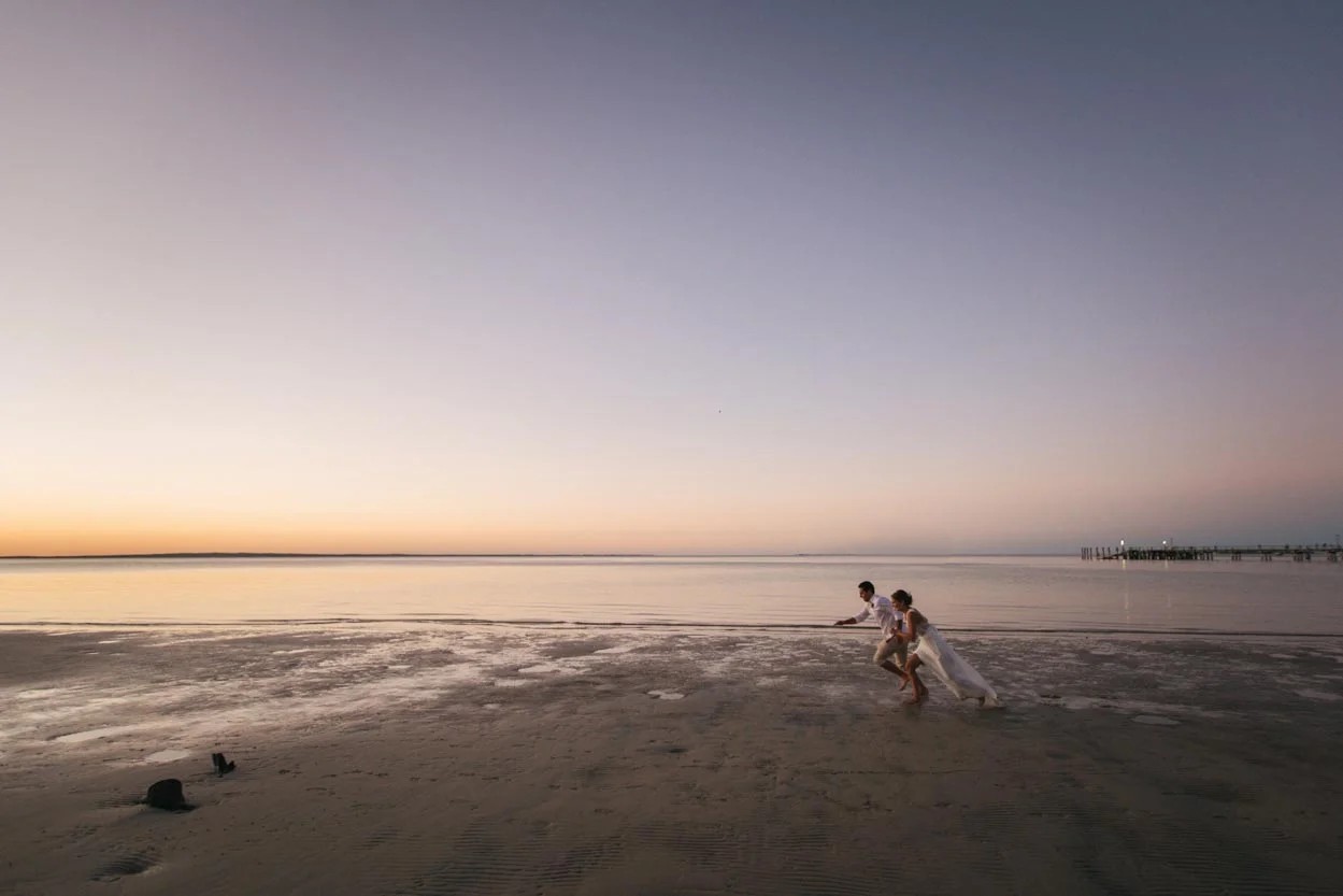 Bride and groom walking along Honeymoon Island shore